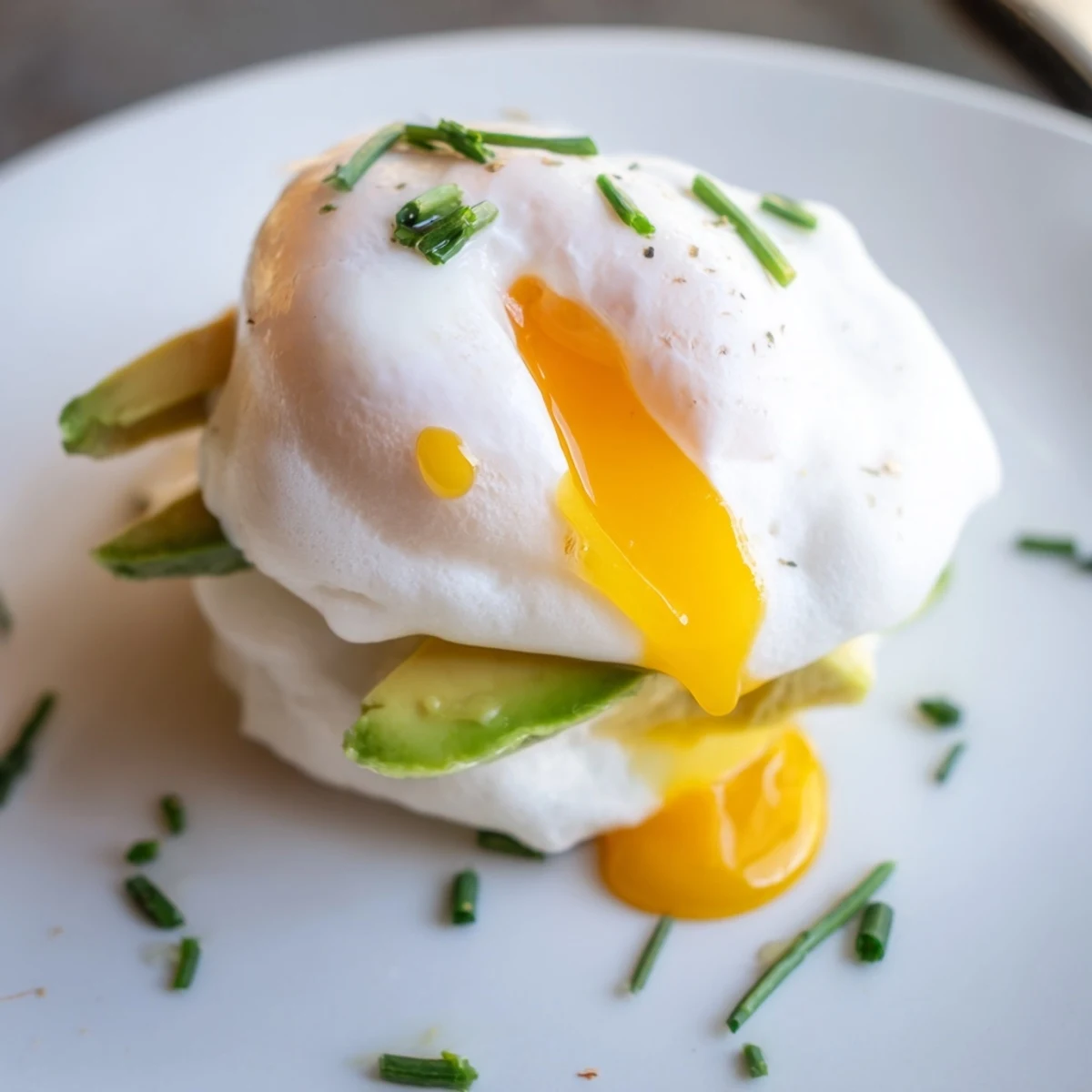Served on a white plate, these Cloud Bread Breakfast Clouds feature pillowy egg whites, runny poached yolks, and vibrant green avocado.