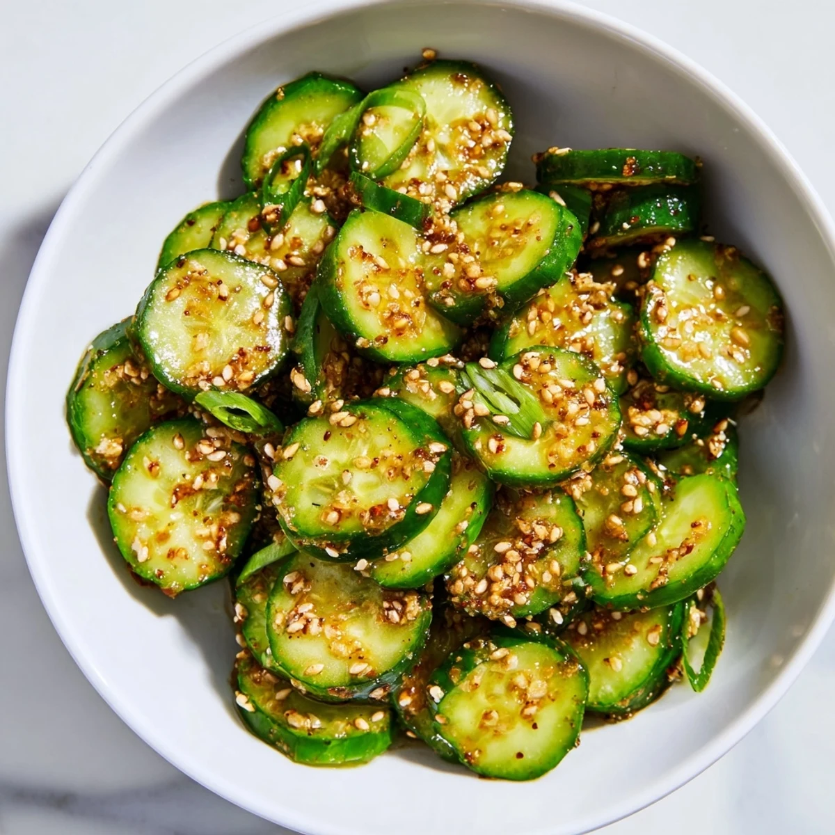 Shake Shake Garlic Cucumbers in a clear glass jar, showcasing glossy, freshly coated slices with a sprinkle of sesame seeds and green onions for a refreshing vegan side dish.  
