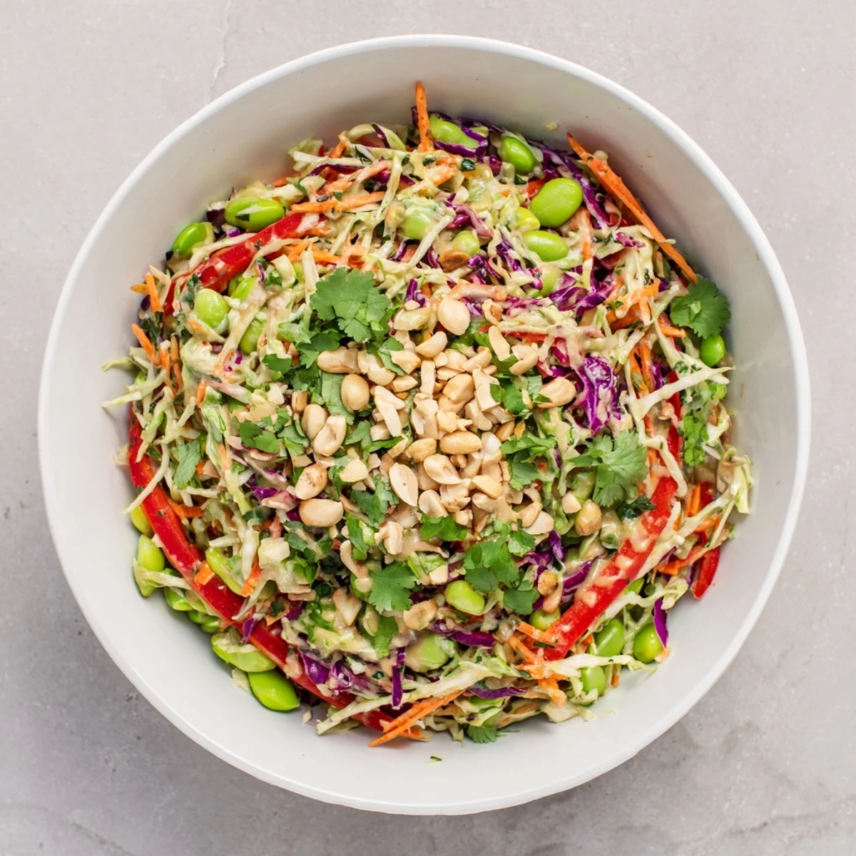 A vibrant bowl of Crunchy Thai Peanut Salad, packed with shredded carrots, cabbage, and edamame, drizzled with creamy peanut dressing.  