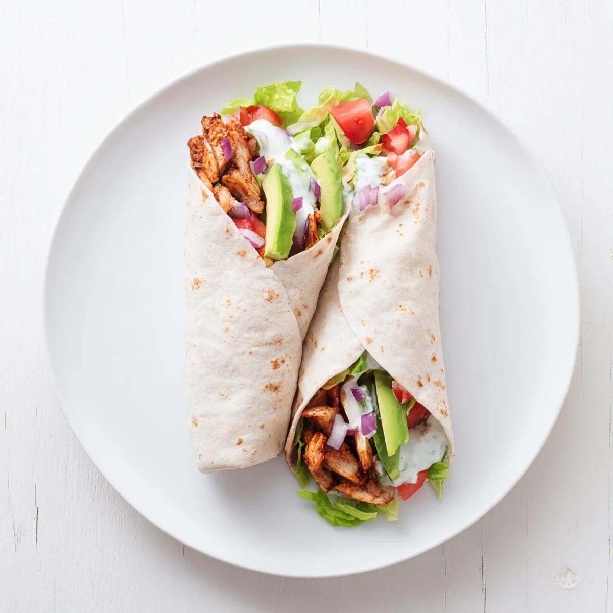 Golden-brown, smoky chipotle chicken wrap sliced in half, revealing layers of creamy avocado, crisp romaine lettuce, and fresh red onion inside a soft tortilla.