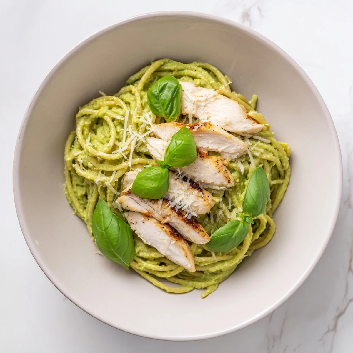 Overhead view of Creamy Avocado Chicken Pasta in a serving bowl, highlighting the creamy green sauce and juicy grilled chicken pieces.