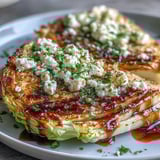 A close-up of crispy cabbage steaks topped with creamy feta and fresh parsley, drizzled with tangy balsamic reduction.