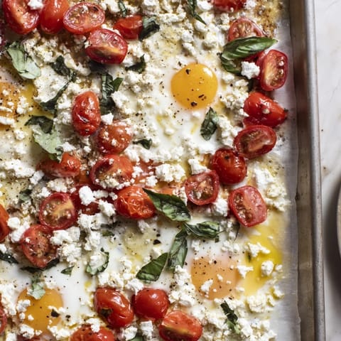 Baked Tomato Feta Eggs on a sheet pan, with runny yolks and fresh basil.