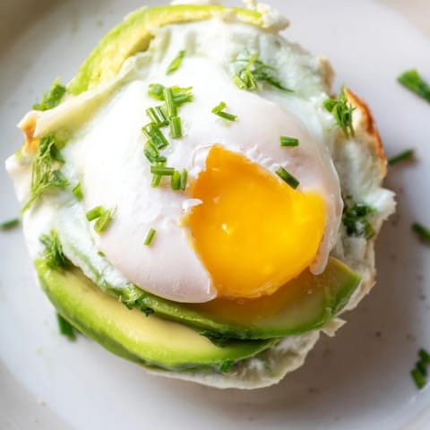 A close-up of poached eggs and avocado on fluffy Cloud Bread Breakfast Clouds, garnished with fresh chives and a sprinkle of red pepper flakes.