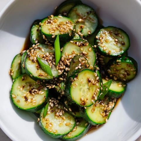 Crisp, vibrant green cucumber rounds glisten with a savory garlic-soy-sesame dressing, perfect for shaking and serving as an easy Asian-inspired appetizer.  