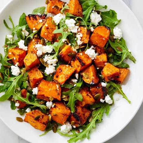 A vibrant Roasted Sweet Potato Salad topped with crumbled feta, sliced red onion, and toasted pumpkin seeds for crunch.