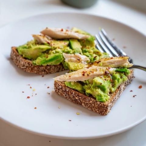 Perfectly grilled chicken slices rest on bright avocado mash on crispy toast, finished with chili flakes and honey.  