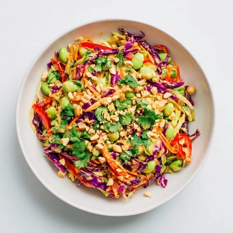 Freshly tossed Crunchy Thai Peanut Salad featuring crisp vegetables, toasted peanuts, and lime wedges on a colorful serving platter.  