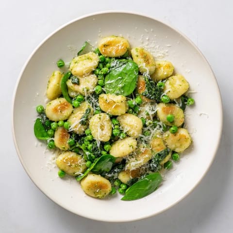 Golden pan-fried gnocchi with vibrant green peas and fragrant basil pesto in a sizzling skillet, ready to serve.