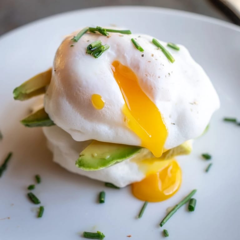 Served on a white plate, these Cloud Bread Breakfast Clouds feature pillowy egg whites, runny poached yolks, and vibrant green avocado.