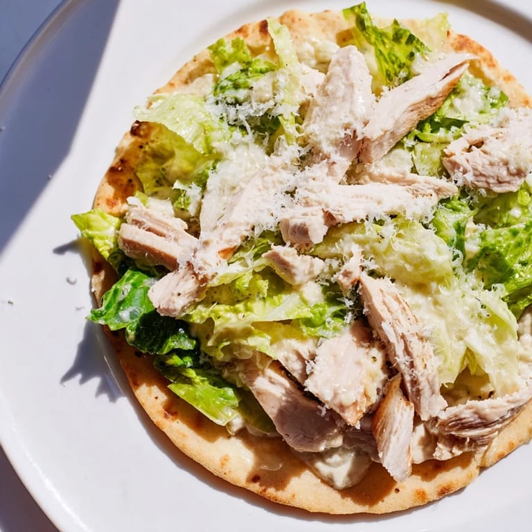 Warm, crispy Chicken Caesar Flatbread plated with tender grilled chicken, crisp lettuce, parmesan shavings, and a side of dressing.